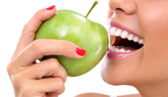 closeup of the face of a woman eating a green apple, isolated against white background